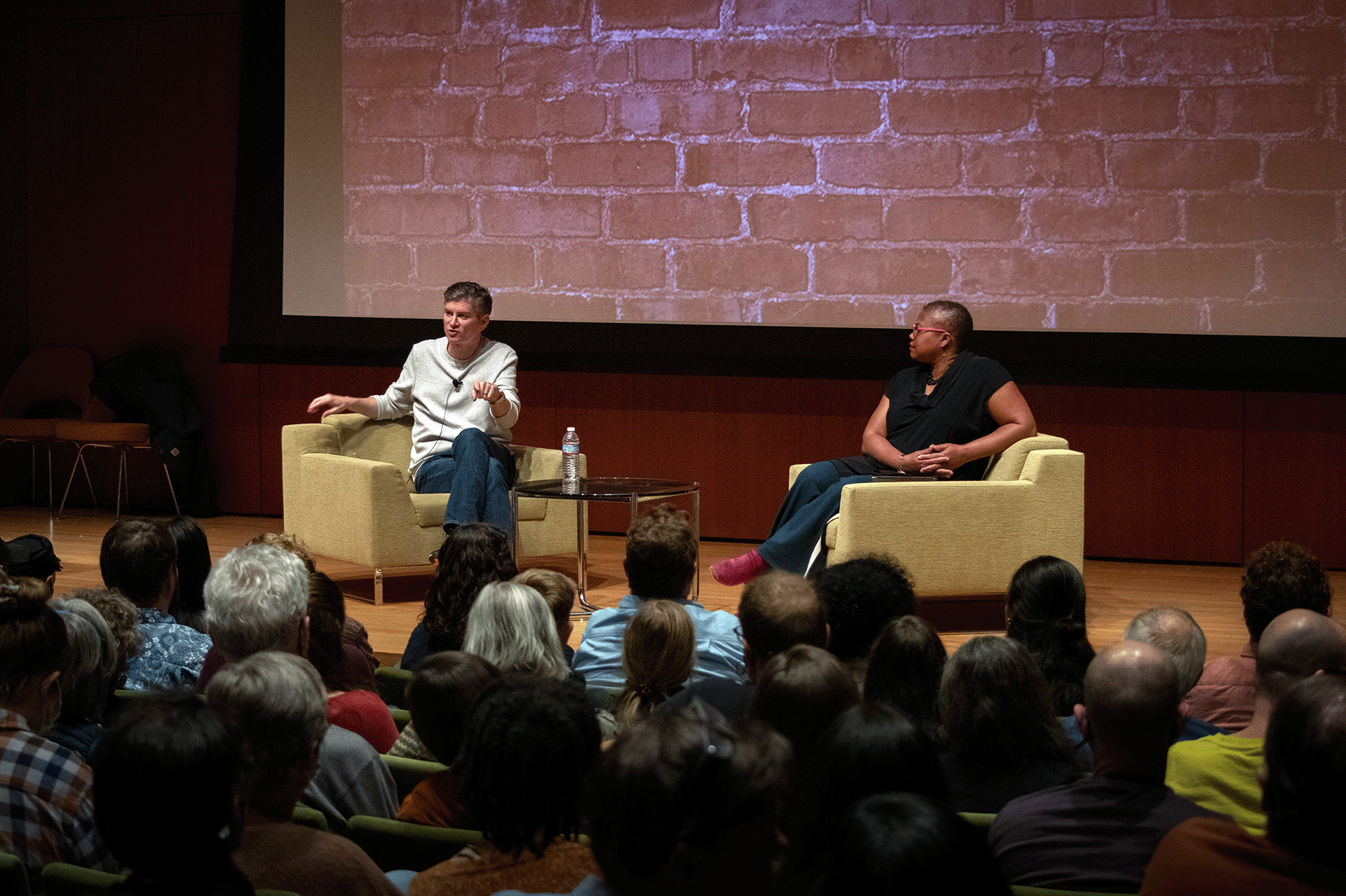 Michael Schur and Adriane Lentz-Smith sit in armchairs on the stage of the Nasher Museum of Art lecture hall in front of a full audience