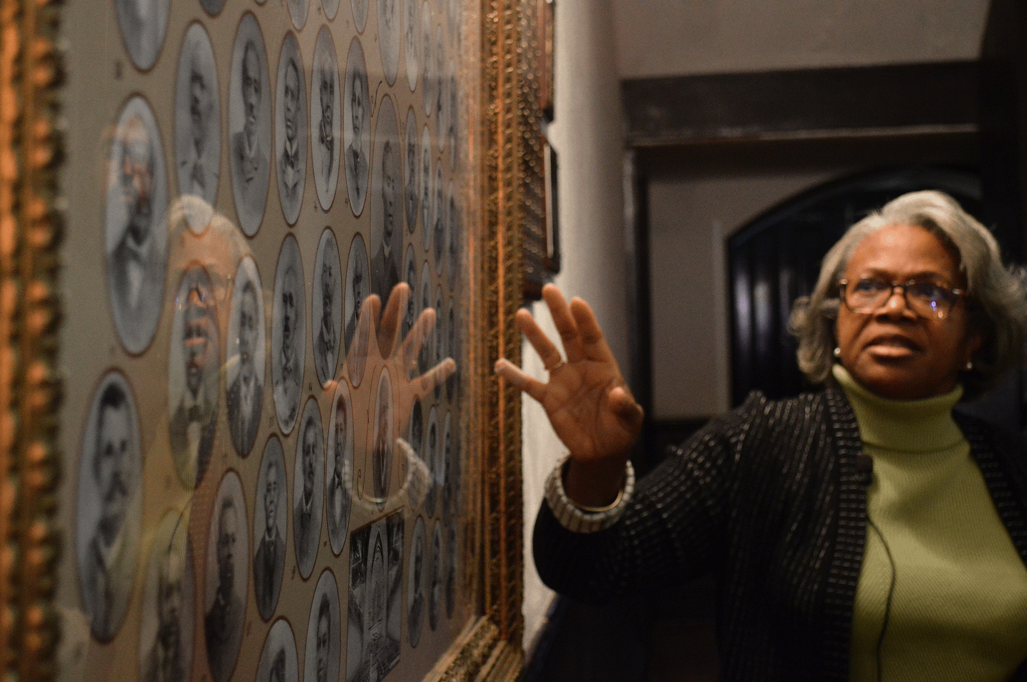 A woman gestures towards a framed picture showing a number of historical portraits
