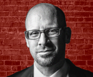 Black and white headshot of Jonathan Metzl against red brick background. 