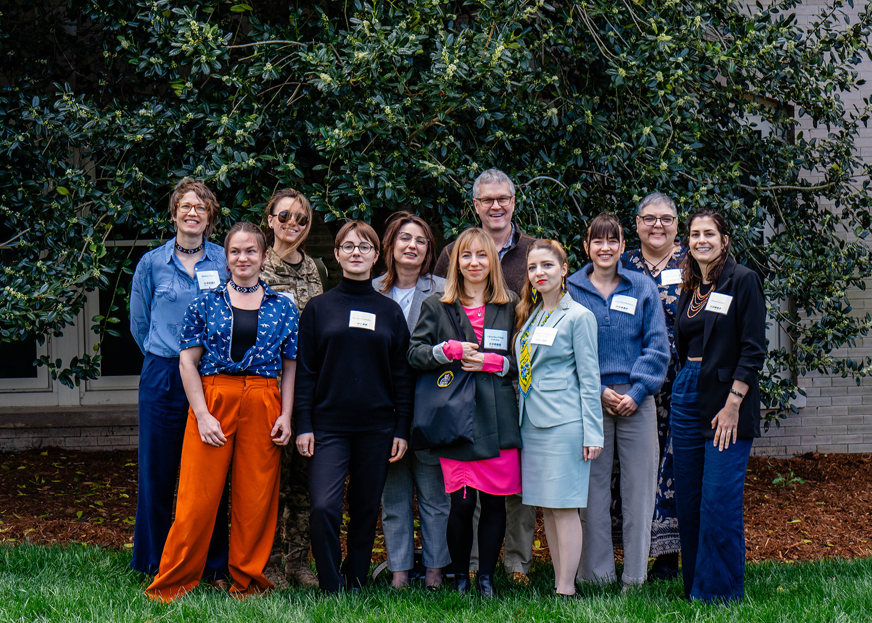 A group of people smile as they stand on the grass in front of a tree.