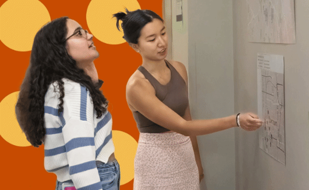 Two students pointing at a display with brightly colored elements behind them