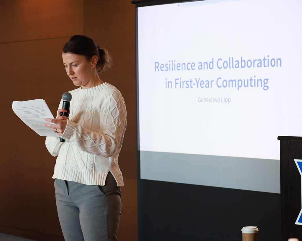 A woman stands in front of a screen reading "Resilience and Collaboration in First-Year Computing"